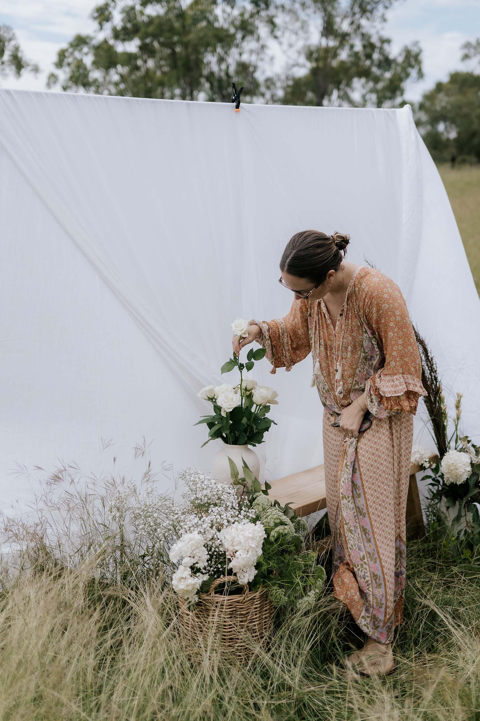 Woman arranging flowers in a field with a white tent in the background